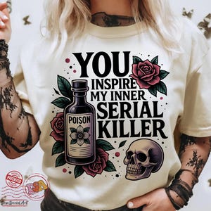 May include: Cream-colored t-shirt with the text "YOU INSPIRE MY INNER SERIAL KILLER" in black. The design includes a poison bottle, roses, and a skull.