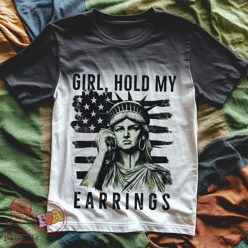 May include: A black and white t-shirt featuring a graphic of the Statue of Liberty holding a phone and the text "Girl, hold my earrings" on a red, white and blue American flag background.