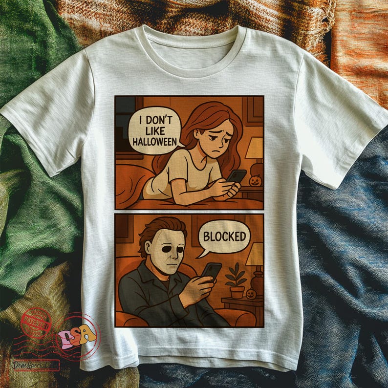 K&ouml;nnte beinhalten: Wei&szlig;es T-Shirt mit Comic-Strip-Design. Das obere Panel zeigt eine Frau mit dem Text "I DON'T LIKE HALLOWEEN". Das untere Panel zeigt einen Mann mit Maske und dem Wort "BLOCKED". Das Design verwendet Braun-, Orange- und Schwarzt&ouml;ne.