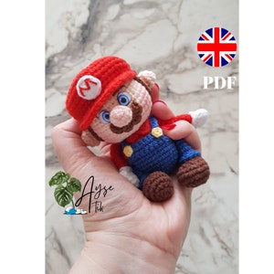 May include: A crocheted Mario figure, featuring a red hat with a white 'M', blue overalls, and a brown mustache. The figure is held in a hand. The image also includes the text 'PDF'.