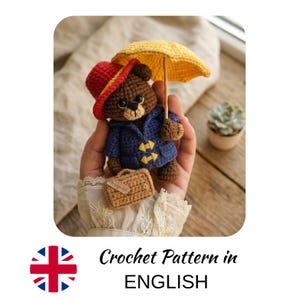May include: A small brown crocheted bear wearing a blue coat with yellow toggles and a red hat. The bear holds a yellow umbrella and carries a small tan suitcase. The text below the image reads Crochet Pattern in ENGLISH.