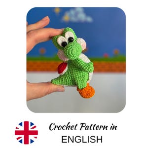 Puede incluir: Una figura de Yoshi tejida a ganchillo en verde y blanco, con una silla de montar roja y zapatos naranjas. La figura está sujeta por una mano. La imagen incluye el texto "Crochet Pattern in ENGLISH".