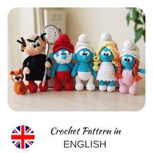 Puede incluir: Una colección de personajes de los Pitufos y un gato hechos a mano con ganchillo. Los Pitufos son azules con gorros blancos, trajes rojos y blancos, y una Pitufina rubia. El gato es naranja. El texto "Crochet Pattern in ENGLISH" está debajo.