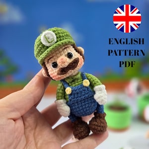 May include: A crocheted Luigi doll, featuring a green hat with a white "L", a brown mustache, and blue overalls. The doll is held in a hand. Text on the image reads "ENGLISH PATTERN PDF".