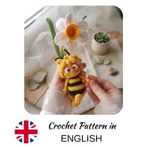 Pode incluir: Uma boneca de crochê feita à mão de um personagem de abelha com listras amarelas e pretas, cabeça redonda e duas antenas, posicionada ao lado de uma flor de narciso de crochê branca e amarela com um longo caule verde, com texturas de fio.