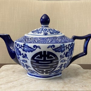 May include: A blue and white porcelain teapot with a floral design and a Chinese symbol. The teapot has a lid and a spout.