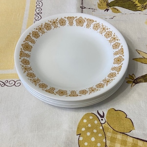 May include: A stack of six white ceramic dinner plates with a gold floral pattern around the rim.