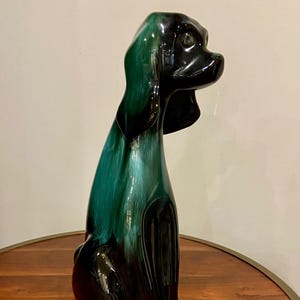 May include: A green and black glazed ceramic dog figurine. The dog is sitting with its head turned to the side. The glaze is a deep green with black accents.