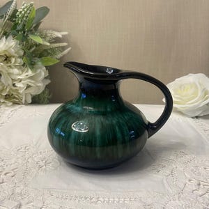 Peut inclure: Un pichet rond vintage avec un glaçage vert foncé et bleu. Le pichet a une anse et un bec verseur. La surface a une finition brillante. Le pichet est un objet décoratif.