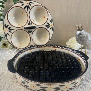 May include: A ceramic serving dish set with a black grill insert and a separate divided plate. The dishes have a cream background with a floral pattern in black, yellow, and red. The set is designed for serving appetizers or small dishes.