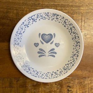 May include: A white ceramic plate with a blue and white speckled pattern around the edge. The centre of the plate features a blue and white heart design with two smaller hearts on either side.