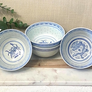 Peut inclure: Trois bols en céramique blanche ornés de motifs peints en bleu. Deux bols présentent des motifs floraux complexes, tandis qu'un bol arbore une illustration détaillée de dragon. Chaque bol possède une bordure géométrique bleue sur le rebord.