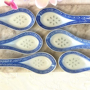 Peut inclure: Six cuillères à soupe en céramique bleu et blanc avec un motif floral dans le bol et un motif géométrique sur le manche. Les cuillères sont disposées sur une planche de service en pierre de couleur claire.