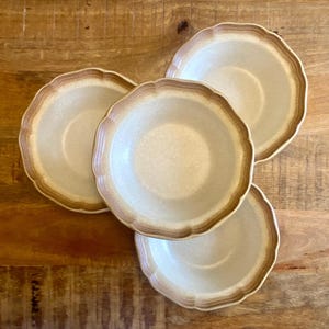 Peut inclure: Un ensemble de quatre bols ronds en céramique avec un bord festonné. Chaque bol présente un centre blanc cassé moucheté et un large bord brun dégradé qui passe d'un ton beige clair à une teinte plus foncée le long de la bordure festonnée.