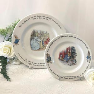 Peut inclure: Deux assiettes en céramique blanche avec des illustrations de lapins et du texte d'une histoire pour enfants. Les assiettes présentent des scènes avec des lapins dans un jardin, avec du texte sur les bords.