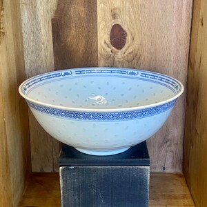 Peut inclure: Un grand bol en porcelaine blanche avec un motif floral et géométrique bleu sur le bord. Le bol présente un design délicat et perforé et est posé sur un support noir sur un fond en bois. Un classique de la vaisselle d'inspiration asiatique.