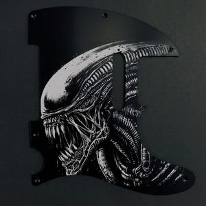 Könnte beinhalten: Schwarzes Gitarren-Schlagbrett mit einer detaillierten weißen Illustration des Kopfes eines Alien-Kreatur. Das Schlagbrett hat eine einzigartige Form mit Schraubenlöchern zur Montage. Das Design bildet einen auffälligen Kontrast zum schwarzen Hintergrund.