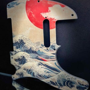 May include: A guitar pickguard with a Japanese wave design and a large red sun. The pickguard is shaped to fit a specific guitar model and has pre-drilled holes for mounting.
