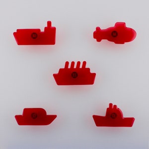 May include: Five red plastic toy vehicles: a ship, a helicopter, a cruise ship, a boat, and a tugboat. Each has a circular design in the centre. The toys are arranged on a white background.