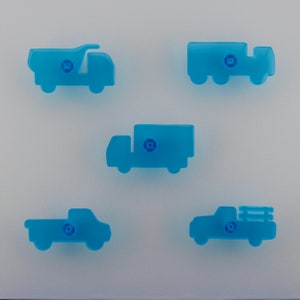 May include: Five light blue truck-shaped cabinet knobs. The knobs are in different styles, including a dump truck, a semi-truck, and a pickup truck. Each knob has a small, round, darker blue centre.