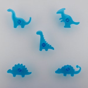 Peut inclure: Cinq figurines de dinosaures en plastique bleu. Les dinosaures sont un stégosaure, un brachiosaure, un tricératops, un vélociraptor et un ankylosaure.