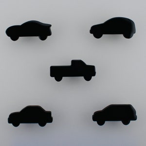 Peut inclure: Cinq objets noirs en forme de voiture sont disposés sur un fond blanc. Les voitures comprennent un coupé, une berline, un pick-up et un SUV. Les objets sont noirs et semblent être faits d'un matériau lisse.