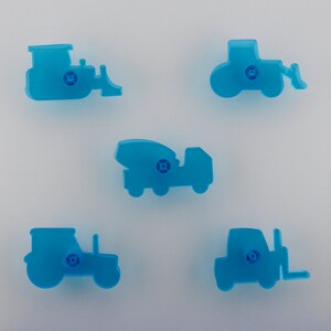 May include: Five light blue plastic cookie cutters shaped like construction vehicles: a bulldozer, a tractor with a front loader, a cement mixer truck, a tractor, and a forklift. Each cutter has a small, circular detail.