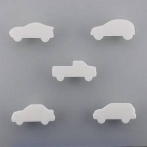 Peut inclure: Cinq objets blancs en forme de voiture sont disposés sur un fond gris. Les véhicules comprennent un coupé, une berline, un SUV et un pick-up. Les objets sont des silhouettes blanches simples et pleines, suggérant un design minimaliste.