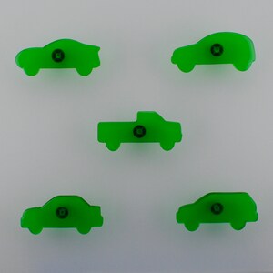 May include: Five green car-shaped cabinet knobs. The knobs are in the shape of a sedan, SUV, pickup truck, and two other car styles. Each knob has a small, dark centre screw.