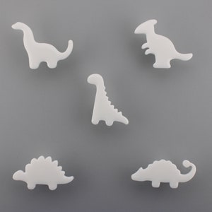 May include: Five white dinosaur shapes, including a stegosaurus, a brachiosaurus, and a tyrannosaurus rex.
