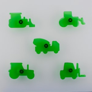 May include: Five green construction vehicle-shaped cabinet knobs. The knobs include a bulldozer, a tractor, a cement mixer, a forklift, and a tractor. Each knob has a black screw in the centre.