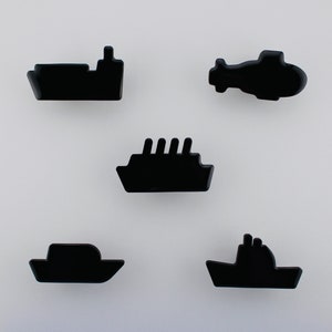 May include: Five black, glossy, miniature transport shapes: a ship, a helicopter, a submarine, a cruise ship, and a boat. The shapes are arranged on a white background. The objects are likely decorative or for a craft project.