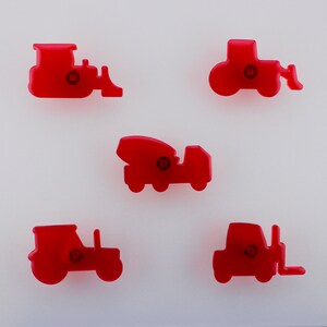 May include: Five red plastic construction vehicle cookie cutters. The set includes a bulldozer, tractor, cement mixer, and two other tractor designs. Each cutter has a small circular detail in the centre.
