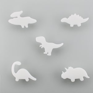 May include: Five white dinosaur shapes on a grey background. The dinosaurs include a Pterodactyl, Stegosaurus, Tyrannosaurus Rex, Brontosaurus, and Triceratops. The shapes are simple and cartoon-like.