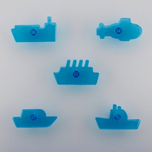 May include: Five translucent blue toy vehicles: a boat, a helicopter, a cruise ship, a small boat, and a tugboat. Each has a small, circular detail in the centre. The toys are arranged on a white background.