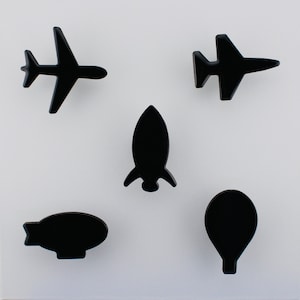 May include: Five black, stylised shapes of transport vehicles are arranged on a white background. The shapes include two aeroplanes, a rocket, a blimp, and a hot air balloon. The objects are solid black and appear glossy.