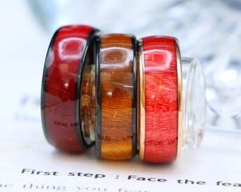 May include: Three wooden rings stacked on top of each other. The top ring is red, the middle ring is brown, and the bottom ring is red with a gold band.