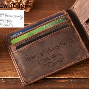 Peut inclure: Un portefeuille en cuir marron avec plusieurs fentes pour cartes, ouvert pour r&eacute;v&eacute;ler des cartes. Le portefeuille est grav&eacute; avec "Happy 8th Anniversary! I love you! Sarah." Une note manuscrite au-dessus dit "Happy 8th Anniversary! I love you! Sarah."