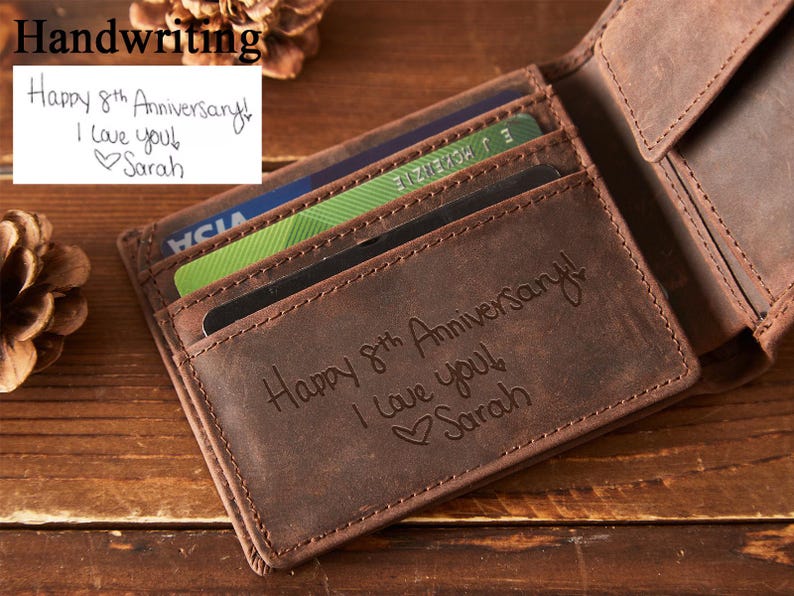 Peut inclure: Un portefeuille en cuir marron avec plusieurs fentes pour cartes, ouvert pour r&eacute;v&eacute;ler des cartes. Le portefeuille est grav&eacute; avec "Happy 8th Anniversary! I love you! Sarah." Une note manuscrite au-dessus dit "Happy 8th Anniversary! I love you! Sarah."