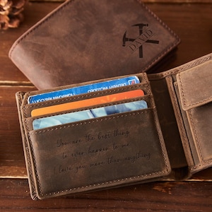 May include: Open brown leather wallet with multiple card slots, displaying credit cards. The wallet is open, revealing a message: "You are the best thing to ever happen to me. I love you more than anything." A second wallet is in the background.