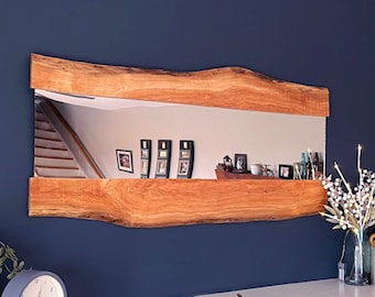 May include: A wooden mirror with a natural edge frame. The mirror is reflecting a staircase and a wall with framed pictures.