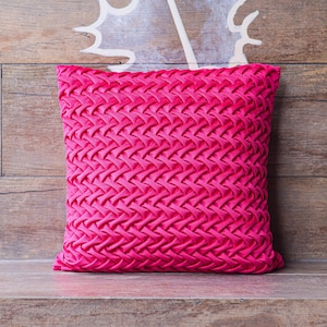 Könnte beinhalten: Ein leuchtend pinkfarbenes Kissen mit einem gewebten Muster. Das Kissen liegt auf einer Holzoberfläche.