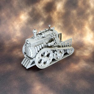 May include: A grey miniature model of a tracked vehicle, resembling a steam-powered engine. The model features detailed components, including a smokestack, gears, and a front grill. The vehicle is set against a mottled brown background.