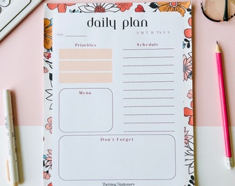 May include: A floral patterned daily planner with sections for date, priorities, schedule, menu, and don't forget. The planner has the text "daily plan" at the top and "Thriving Stationery" at the bottom.