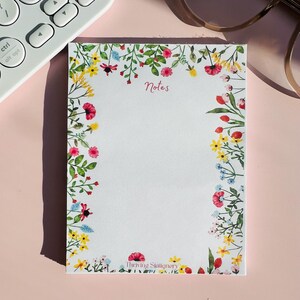 May include: A white notepad with a floral border and the word "Notes" in pink lettering. The notepad has the words "Thriving Stationery" printed at the bottom.