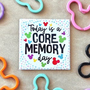 May include: A square magnet with the text "Today is a CORE MEMORY day" surrounded by colorful Mickey Mouse icons and polka dots. The magnet is surrounded by Mickey Mouse-shaped plastic cutouts in various colors.