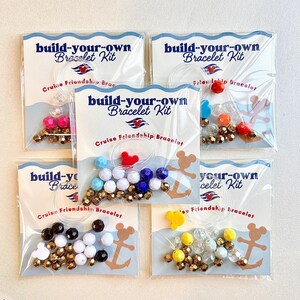 Five packaged build-your-own bracelet kits with different bead color combinations are arranged on a light surface.