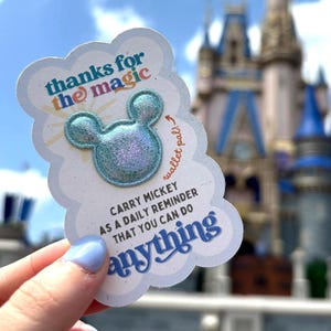 May include: A light blue wallet pal with a Mickey Mouse head design and the text "thanks for the magic." The card also reads "Carry Mickey as a daily reminder that you can do anything."
