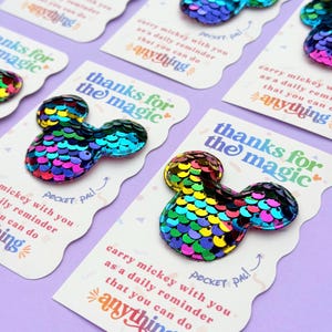 Multiple white cards with rainbow sequin Mickey mouse shapes are arranged in a diagonal pattern on a purple background.