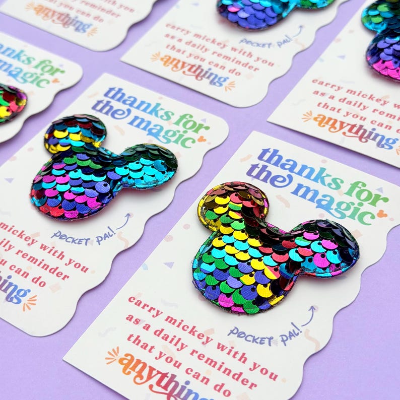 Multiple white cards with rainbow sequin Mickey mouse shapes are arranged in a diagonal pattern on a purple background.